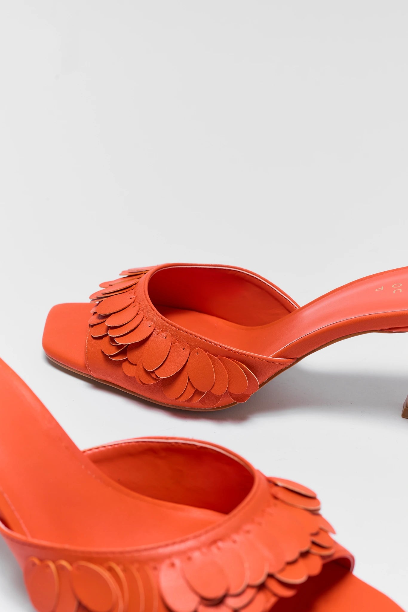 close up Orange high-heeled shoes with scalloped edges on a light gray background