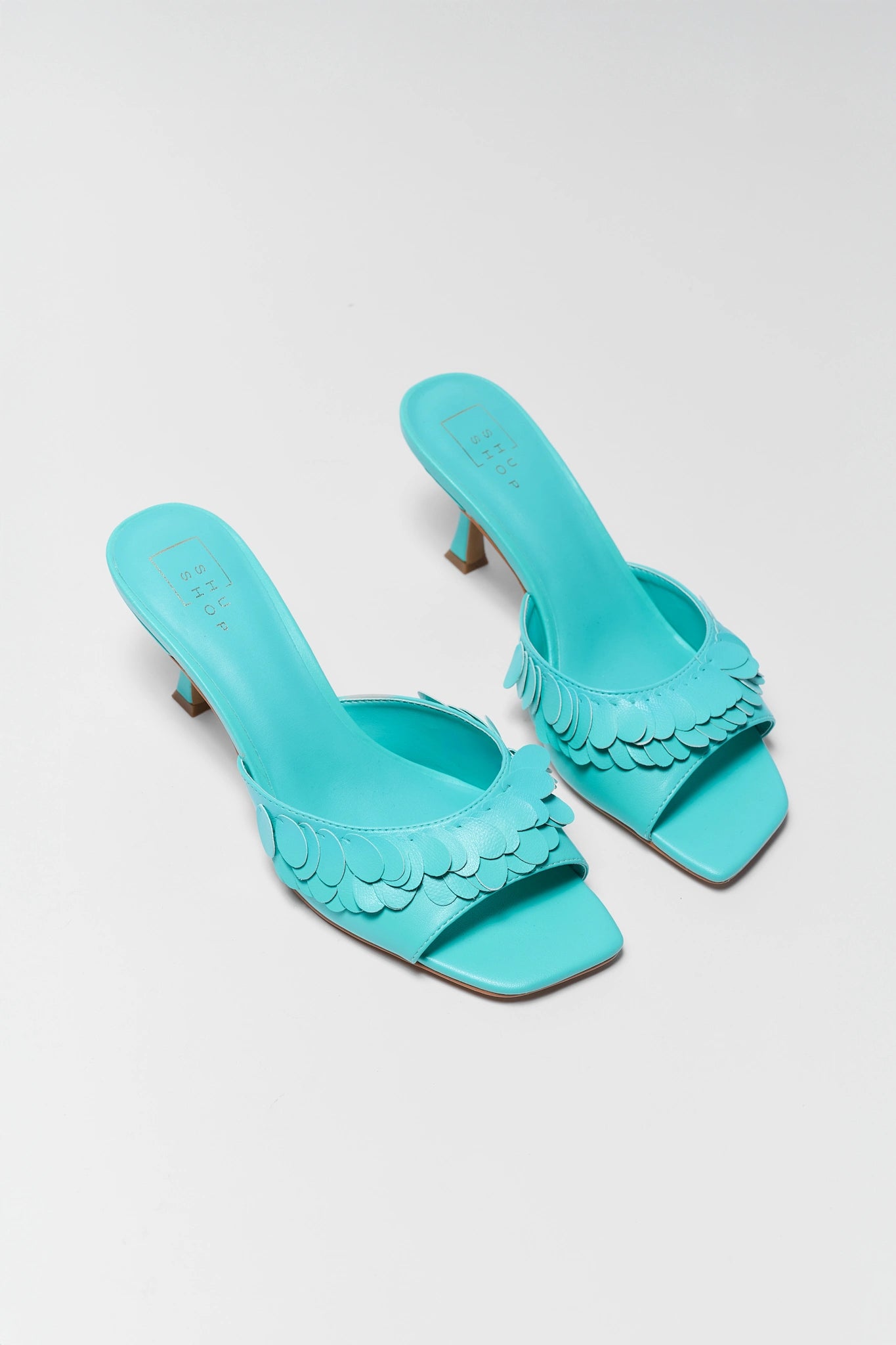 two Pair of turquoise high-heeled sandals with scalloped edges on a light gray background