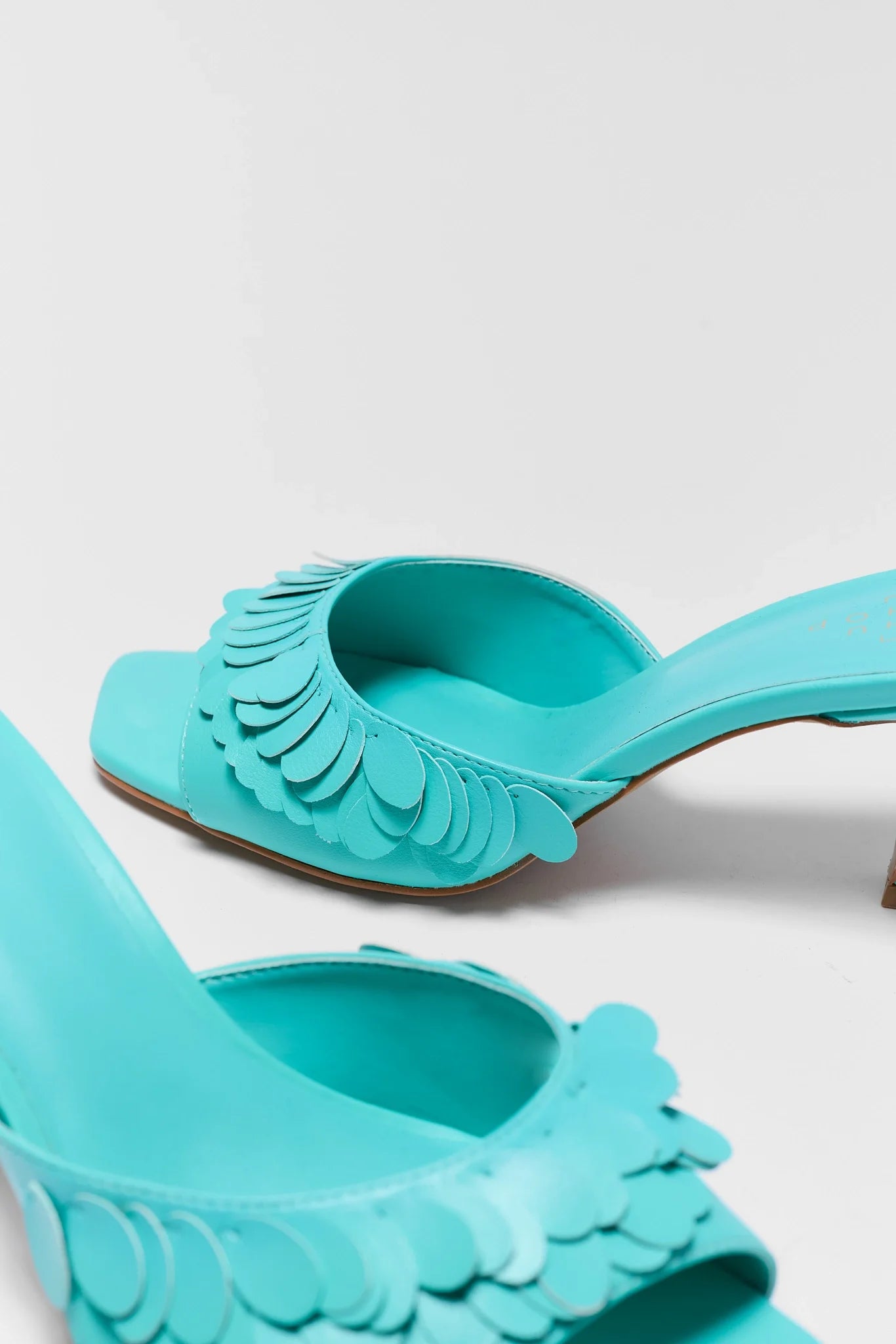 close up Turquoise high-heeled shoes with decorative straps on a light gray background