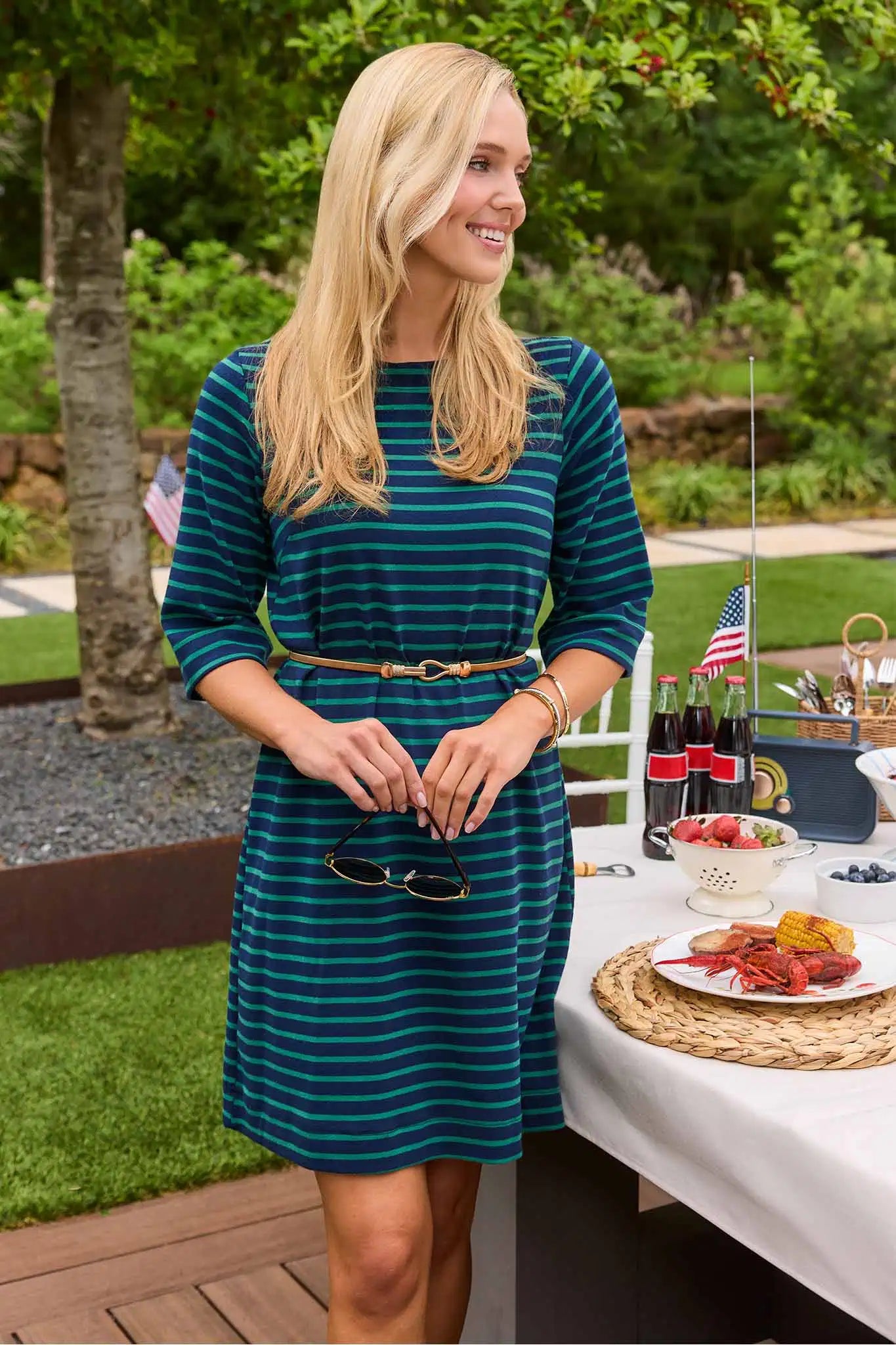 Woman in a blue striped dress standing outdoors near a table with food and drinks.