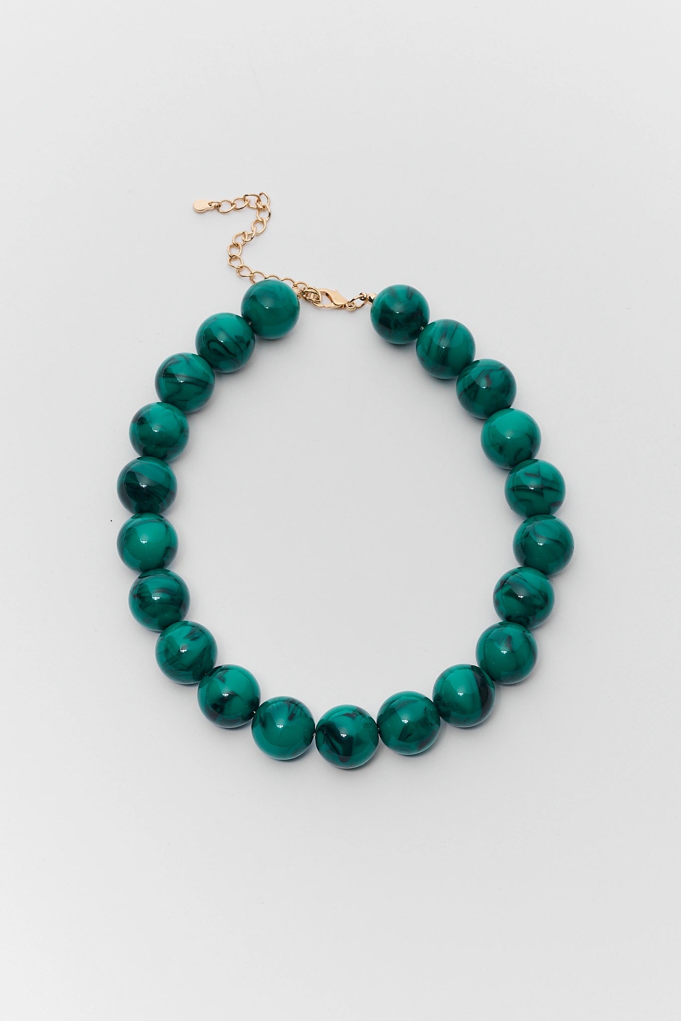 A beaded necklace made of glossy, polished green malachite beads with a gold-tone chain extender clasp, displayed on a neutral light gray background.