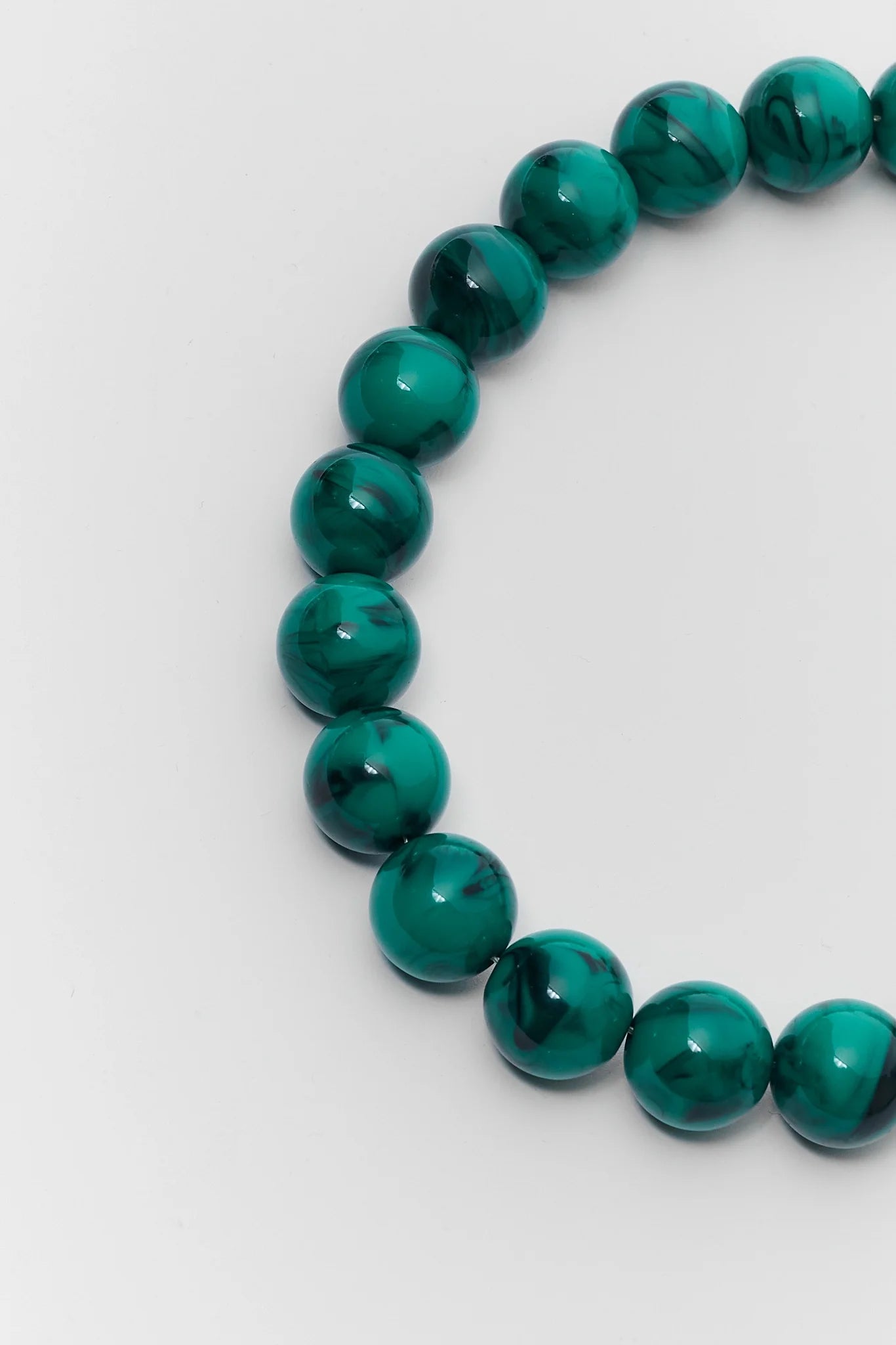 A close-up of a beaded stretch bracelet made of polished round green beads with natural marbled patterns, shown on a light gray background.