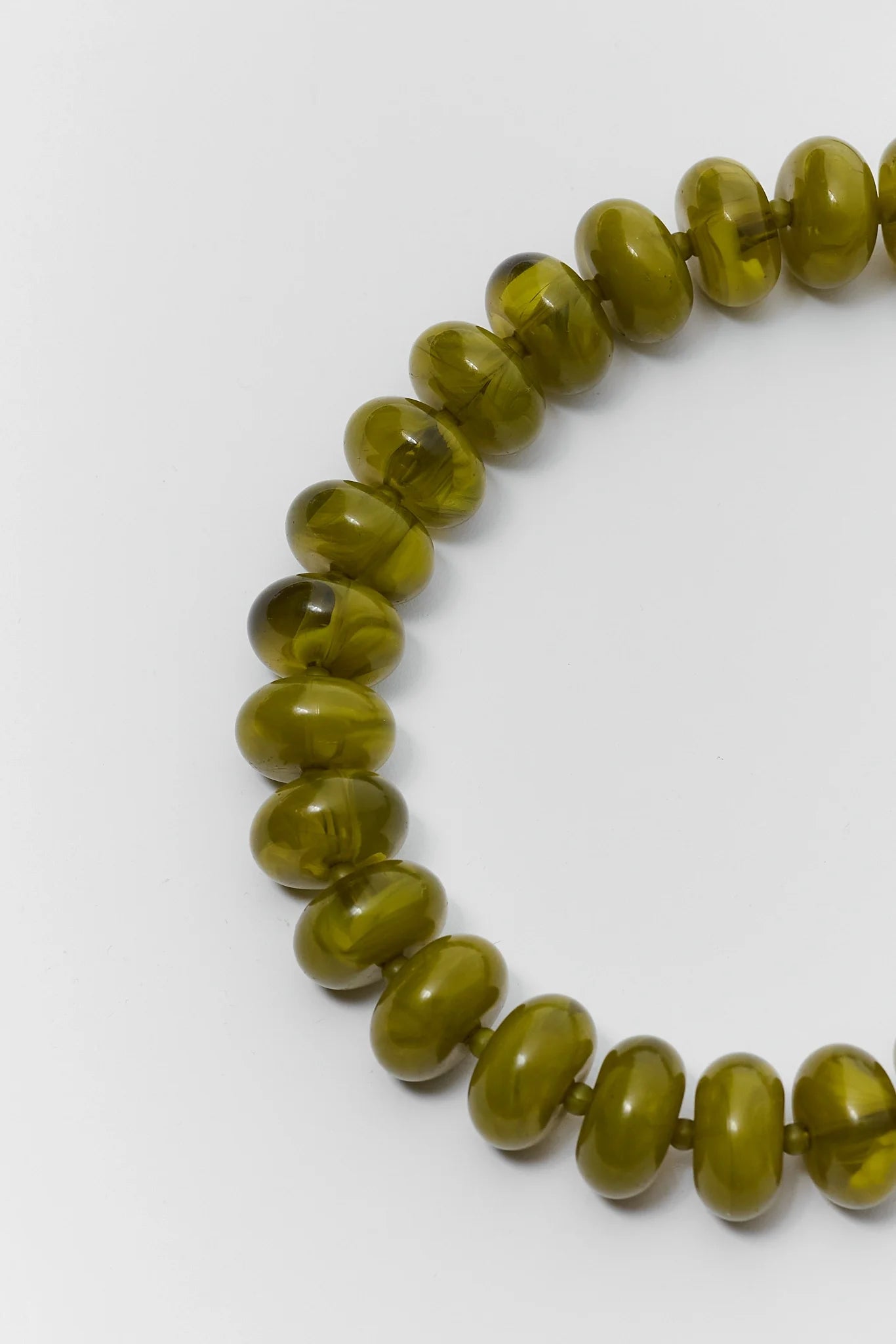 A close-up of a beaded necklace made of glossy, olive-green translucent beads on a plain white background.