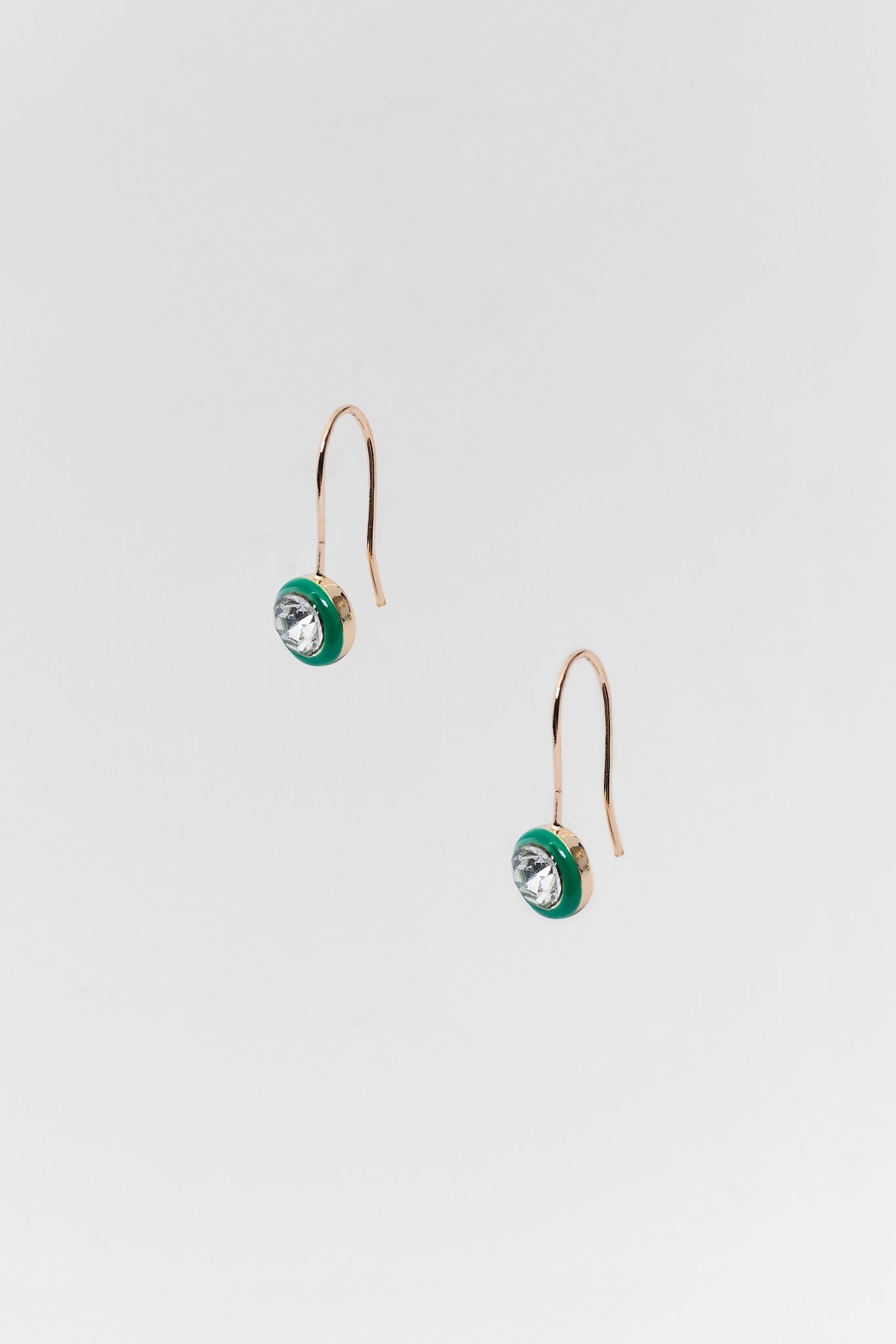 A pair of gold-toned drop earrings with a small circular green and gold charm featuring a clear faceted crystal, shown against a light gray background.