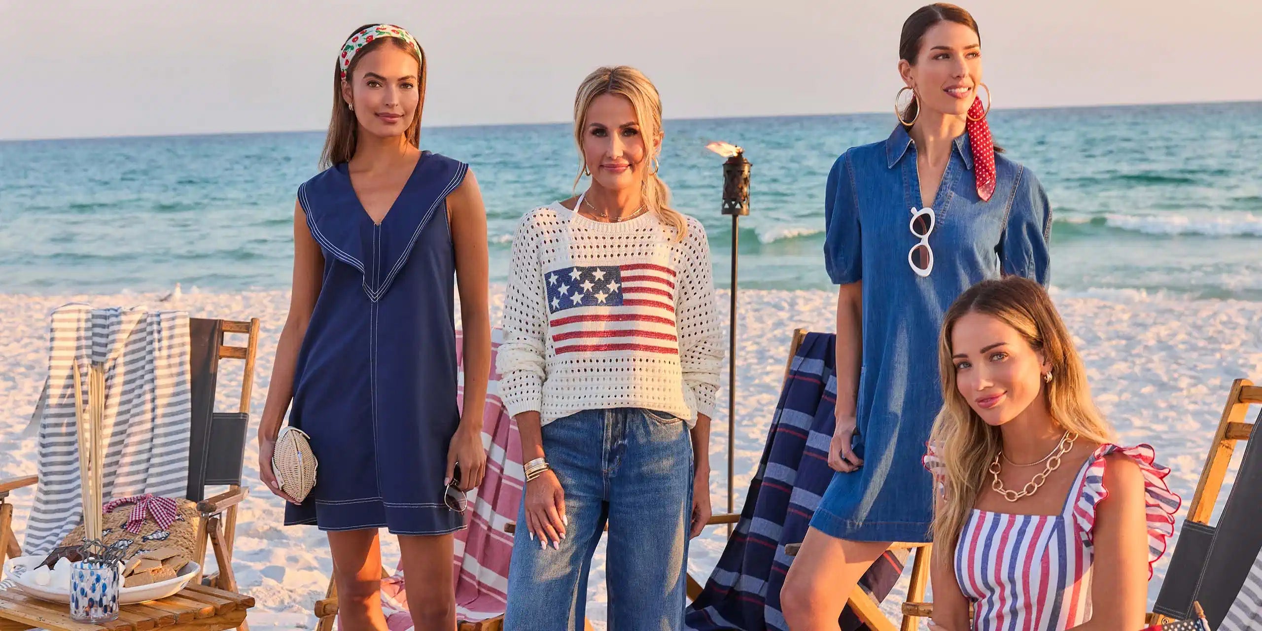 Four women on a beach wearing summer clothing with ocean in the background gated
