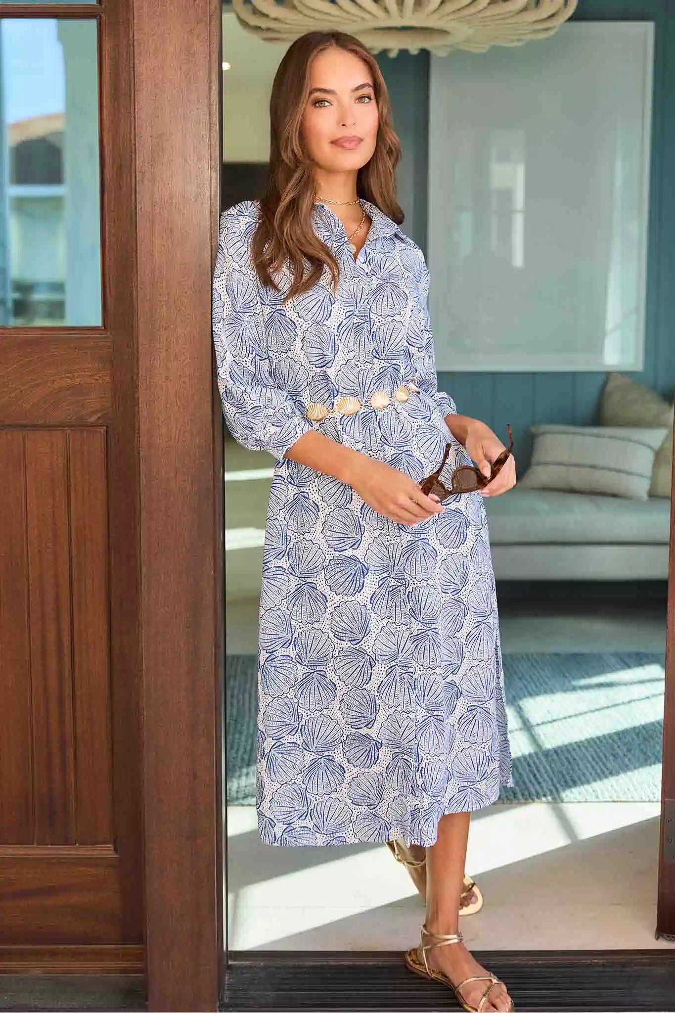 Woman in a blue floral dress standing in a doorway with a modern interior background