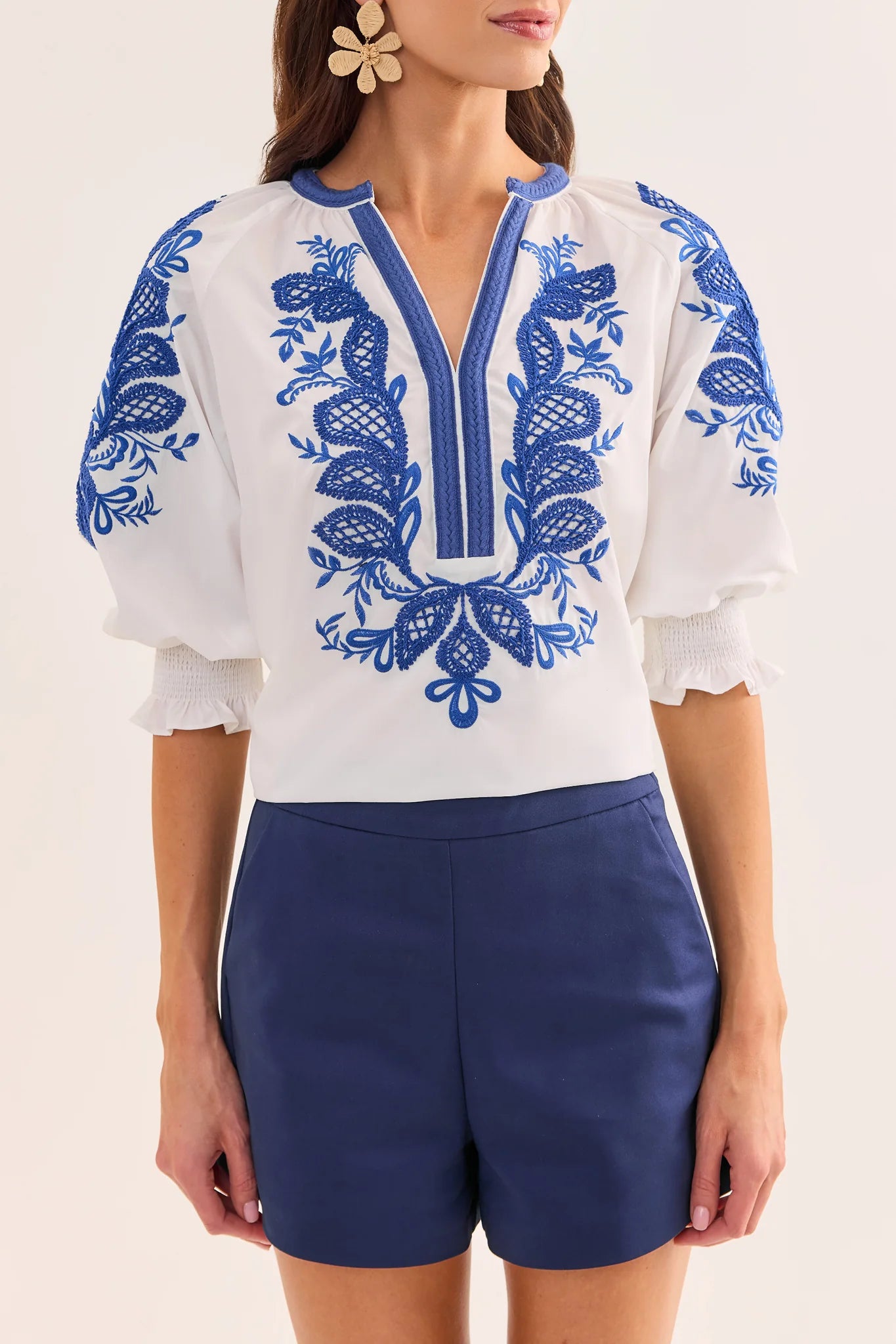 close up Woman wearing a white blouse with blue embroidery and blue shorts on a light background
