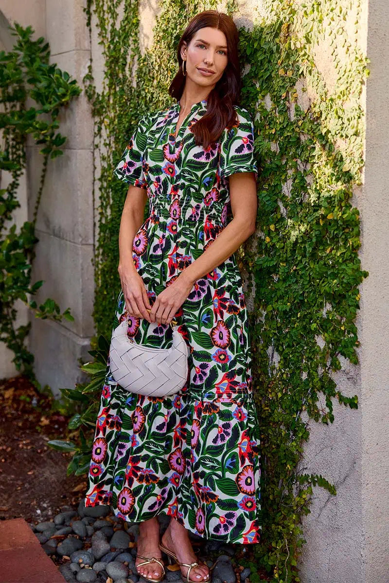 Woman in a floral dress standing against a wall with greenery
