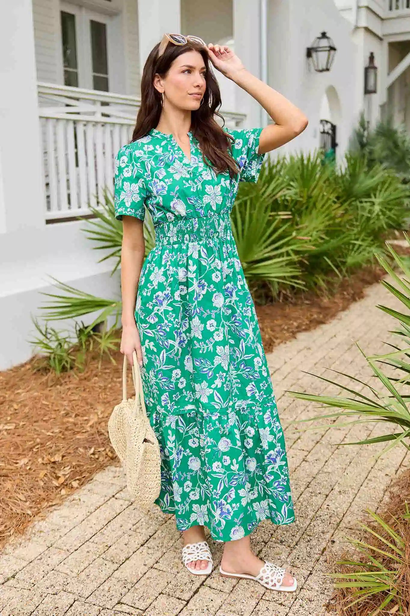 Woman in a green floral dress standing outdoors near a house.