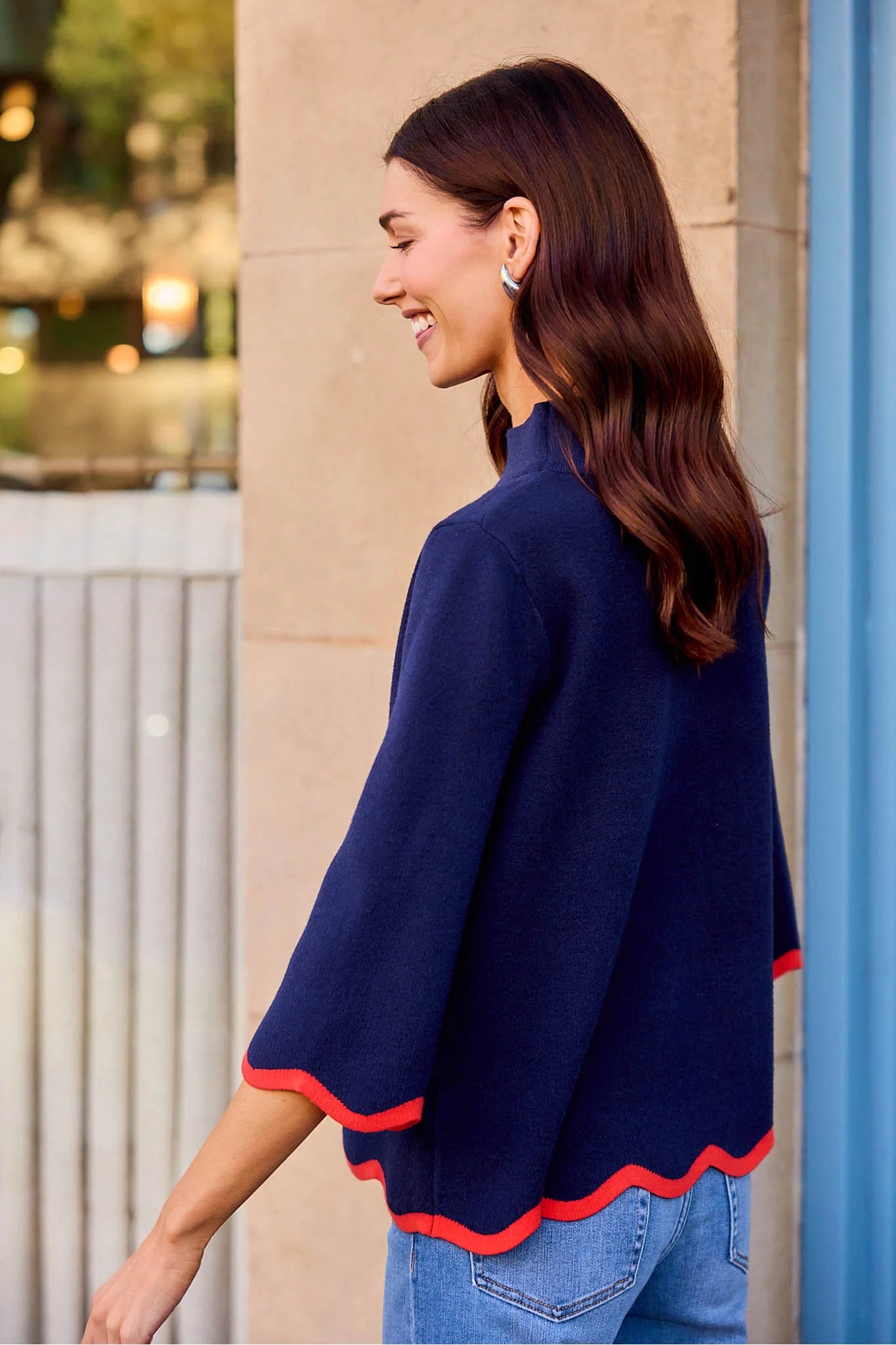 woman walking outside wearing a navy sweater with scallop details 