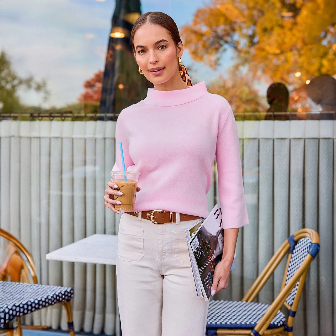 Woman in pink sweater holding a drink and magazine outdoors