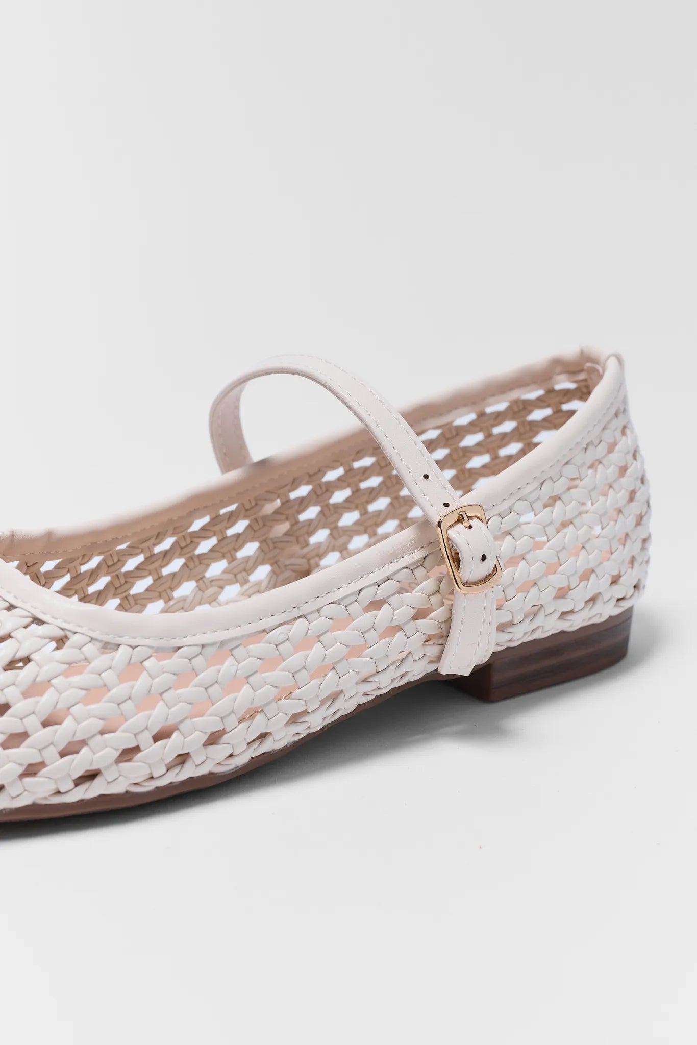 White woven flat shoe with a strap on a light gray background
