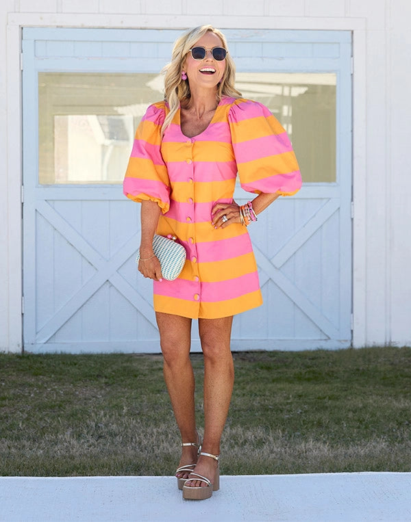 Woman wearing a colorful striped dress standing in front of a white building with blue trim.