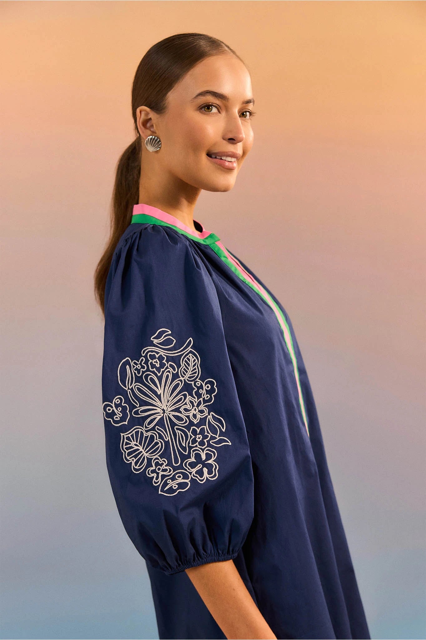 Woman wearing a navy blue dress with floral embroidery against a gradient background