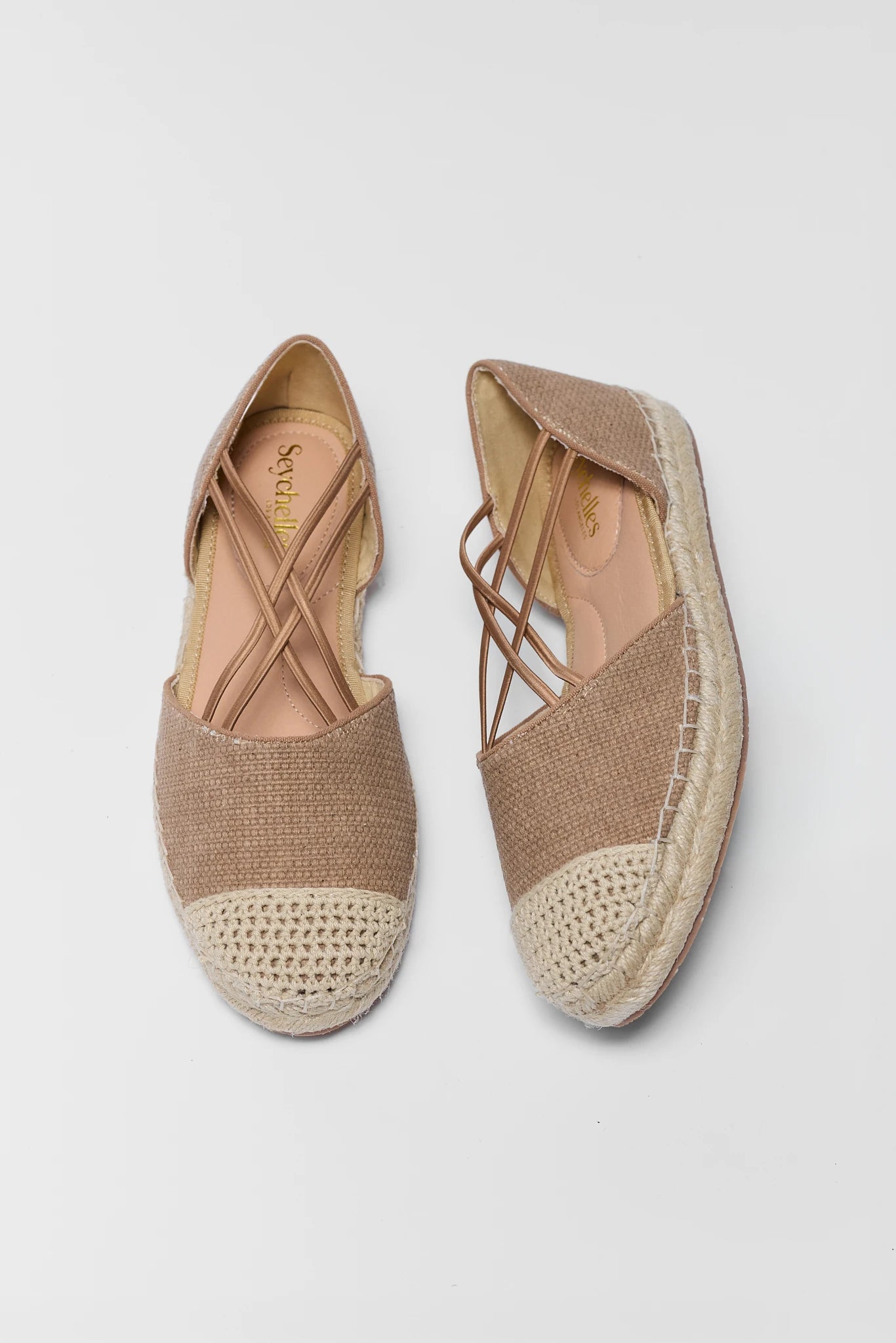Pair of beige espadrilles with woven design on a light gray background