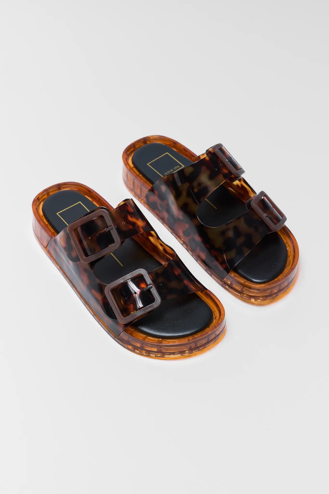 Pair of tortoiseshell sandals with buckle details on a light gray background