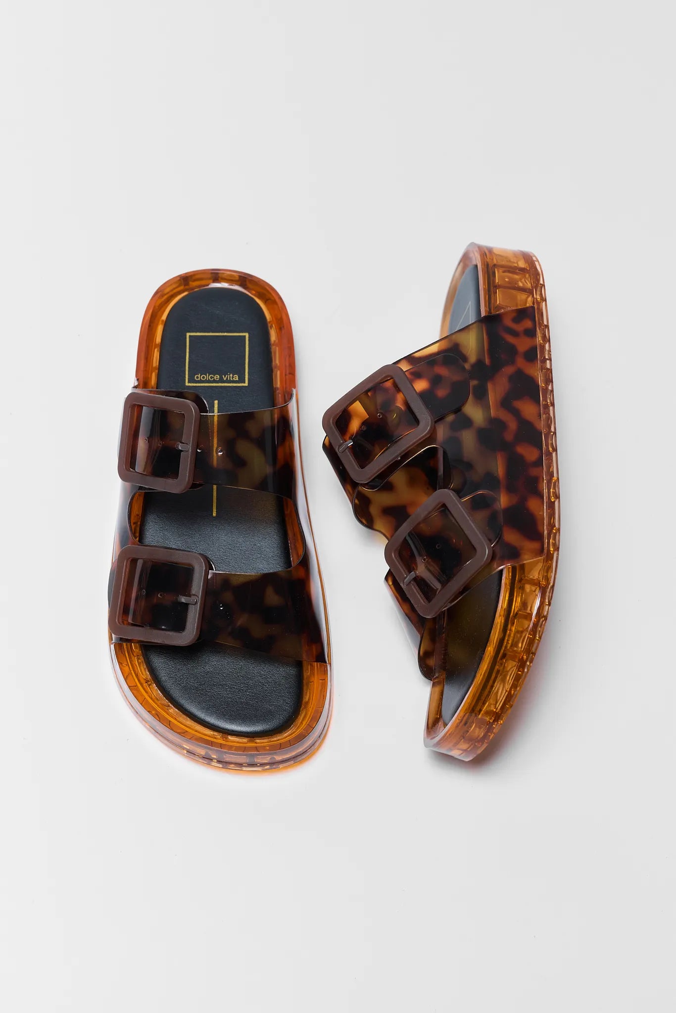 Tortoiseshell sandals with brown buckles on a light gray background