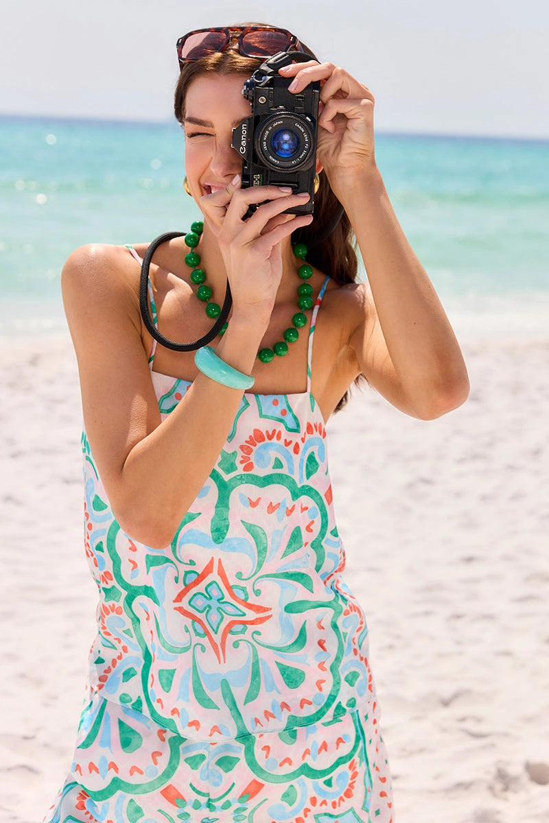 Woman taking a selfie on a beach wearing a colorful dress and green jewelry. mobile