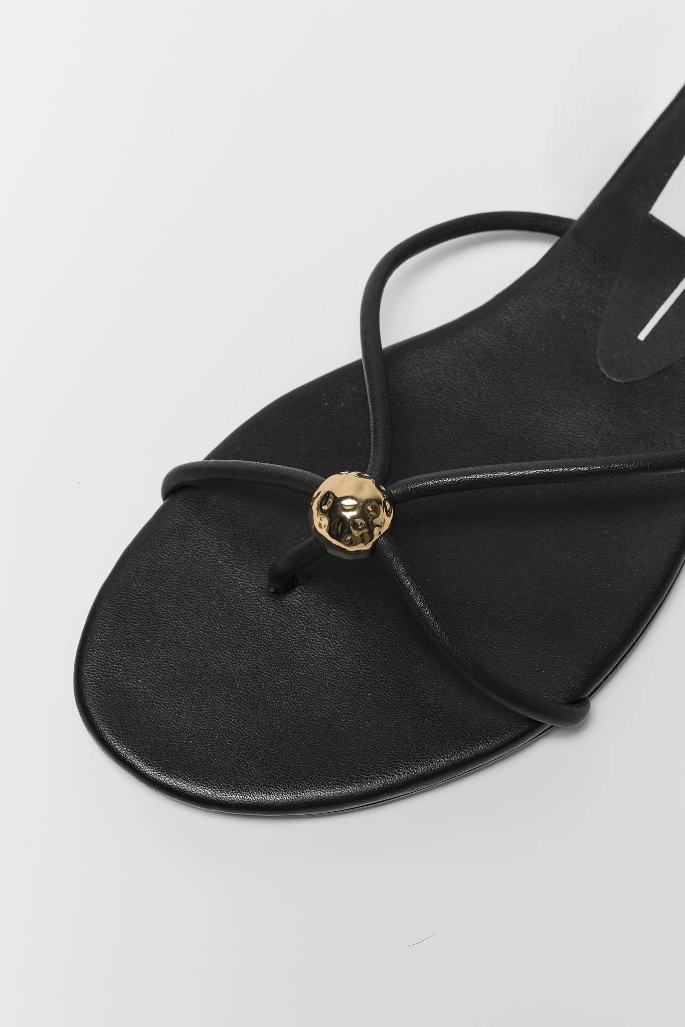 close up Black sandal with a gold embellishment on a white background