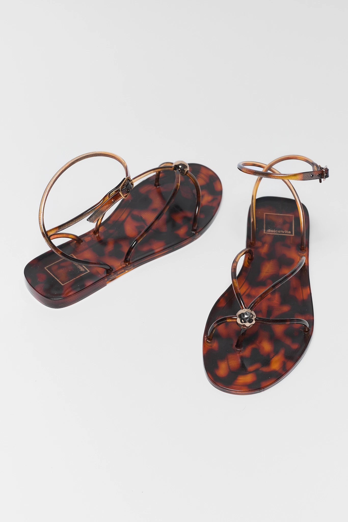 Tortoiseshell sandals with gold straps on a light gray background