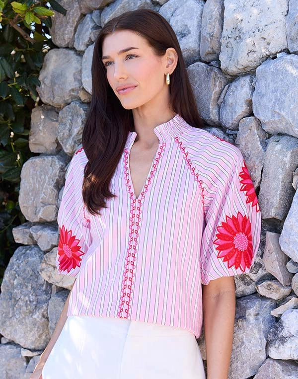 Woman wearing a pink and white striped blouse with floral designs against a stone wall.