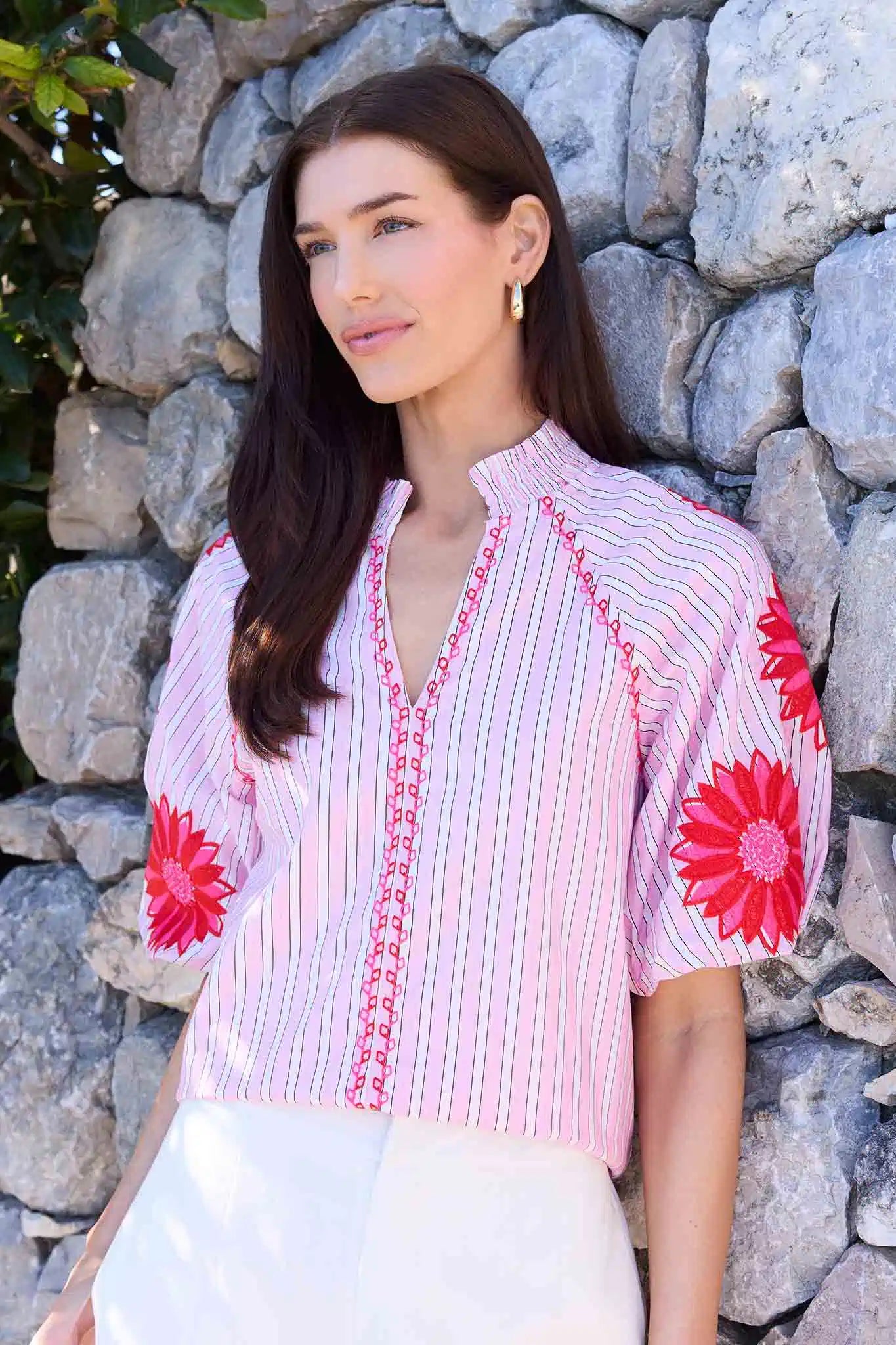 Woman wearing a pink and red floral embroidered blouse against a stone wall.
