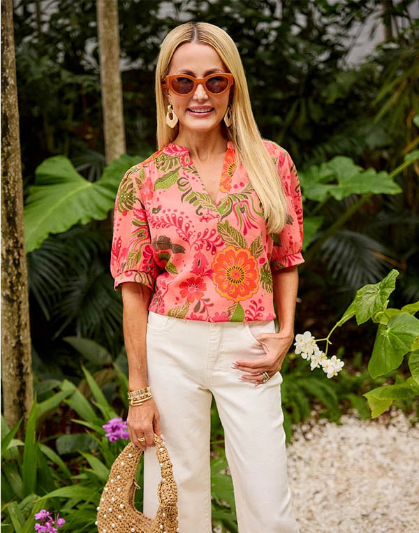Woman wearing a colorful floral blouse and white pants in a tropical setting