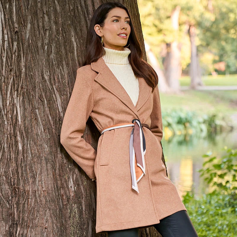 Woman in a beige coat standing by a tree in a park