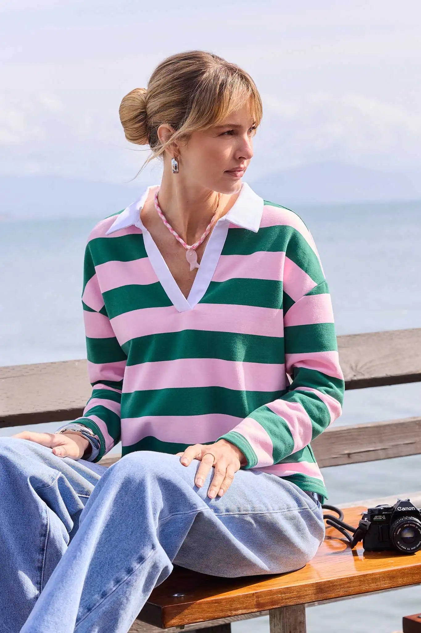 Woman sitting on a bench by the sea wearing a striped sweater.
