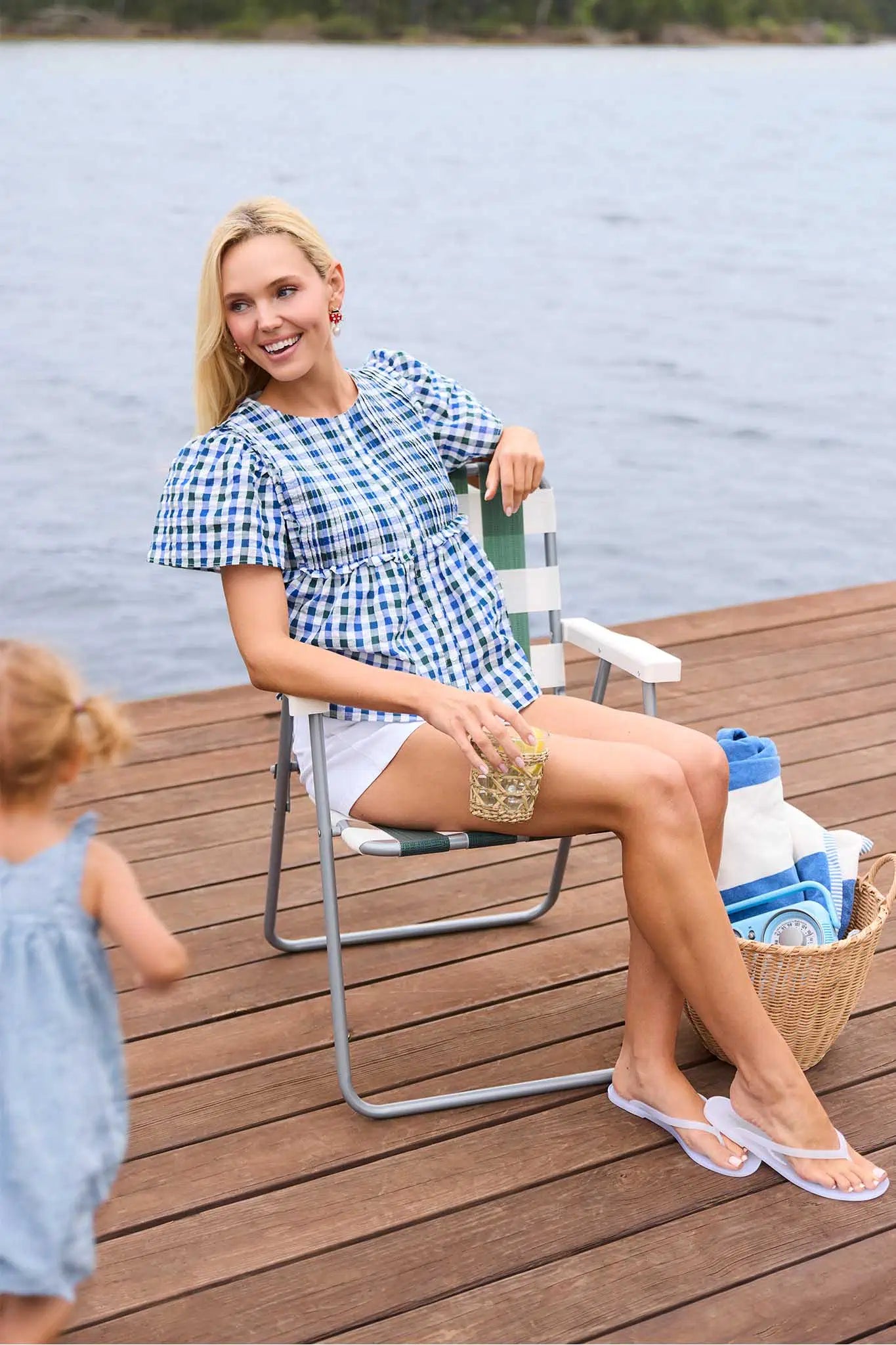 Woman sitting on a chair by a lake with a child and picnic items.