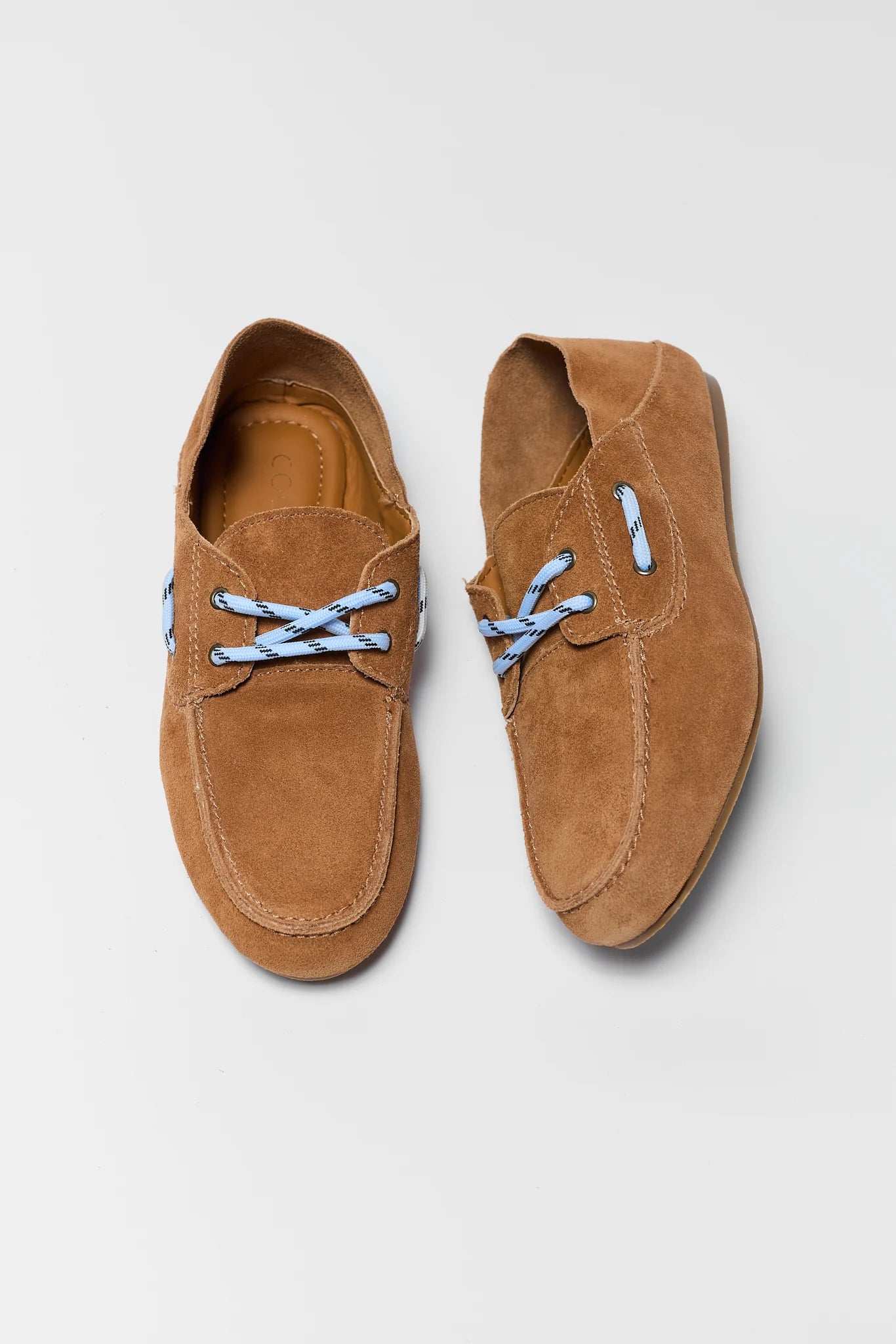 Pair of brown suede shoes with blue laces on a light gray background