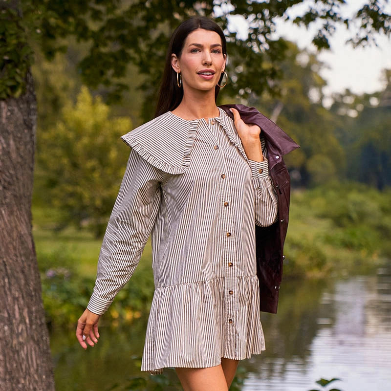 Woman in a striped dress holding a jacket outdoors by a body of water