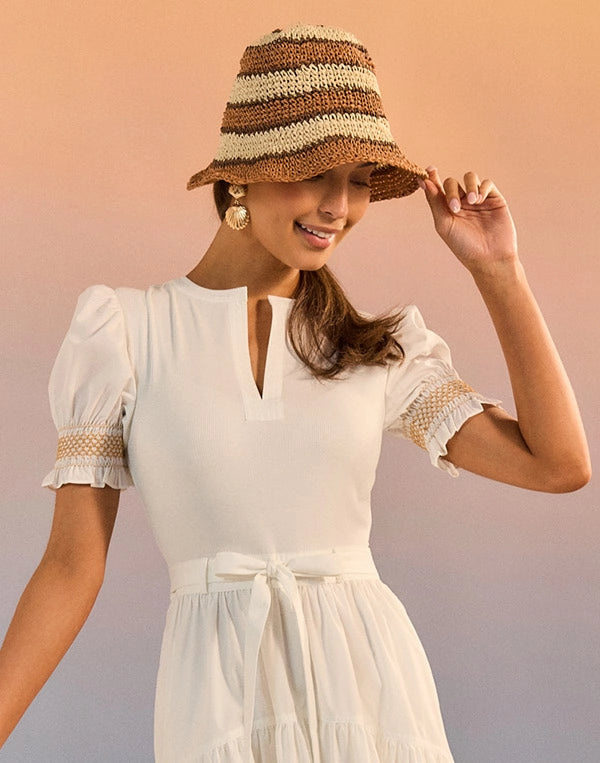 Woman wearing a white dress and striped hat against a gradient background