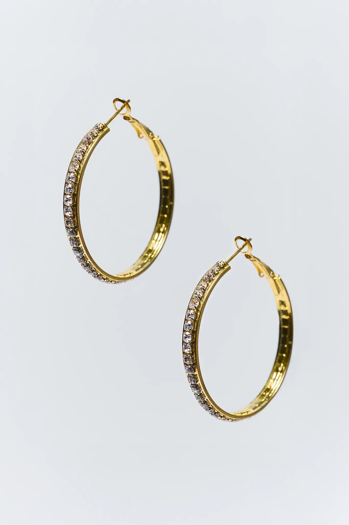 Gold hoop earrings with embedded stones on a light gray background