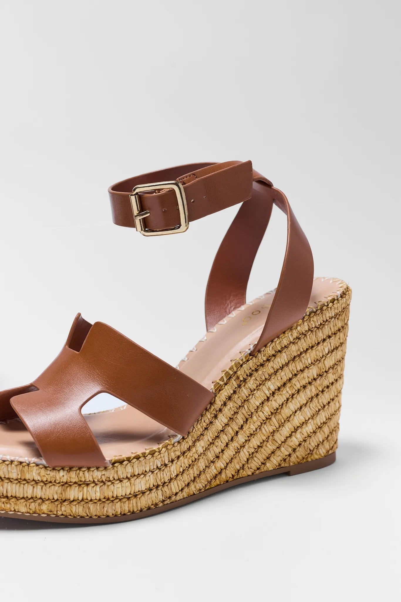 Brown wedge sandal with raffia sole on a light gray background