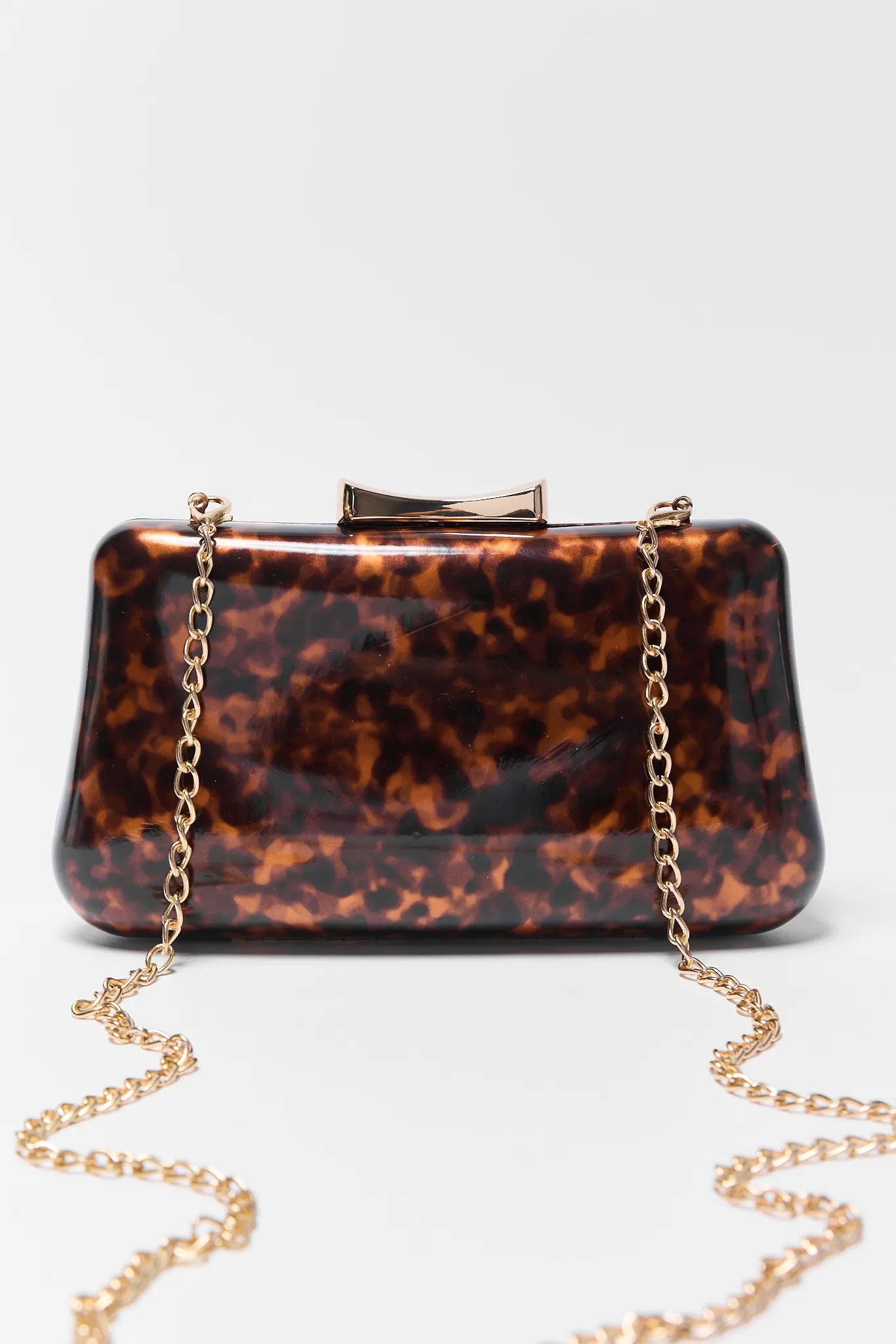 Tortoiseshell handbag with gold chain strap on a light gray background