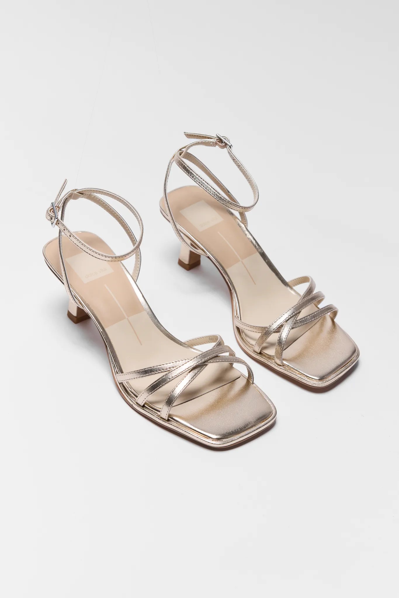 Gold high-heeled sandals on a light gray background