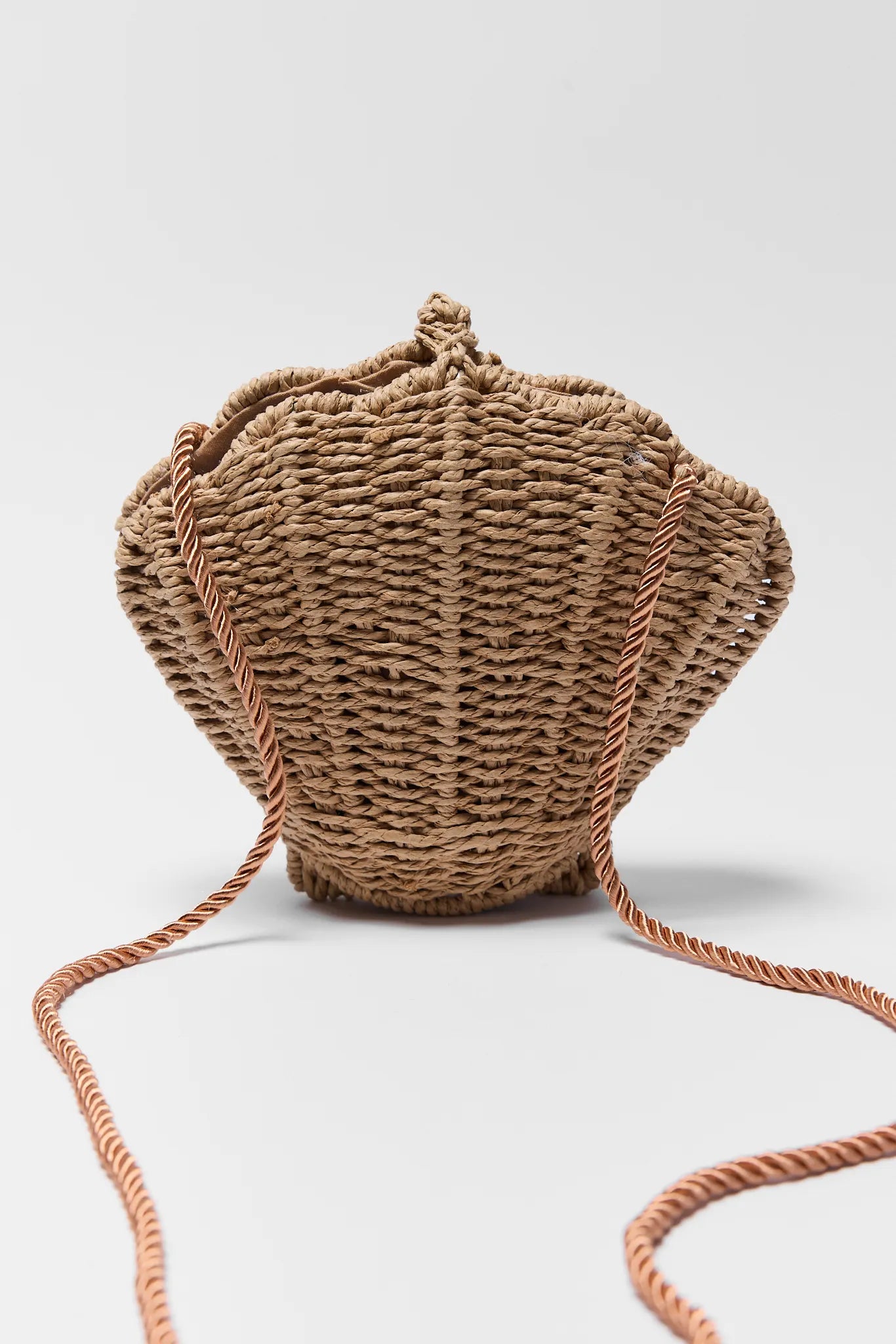 Woven handbag shaped like a seashell on a light gray background