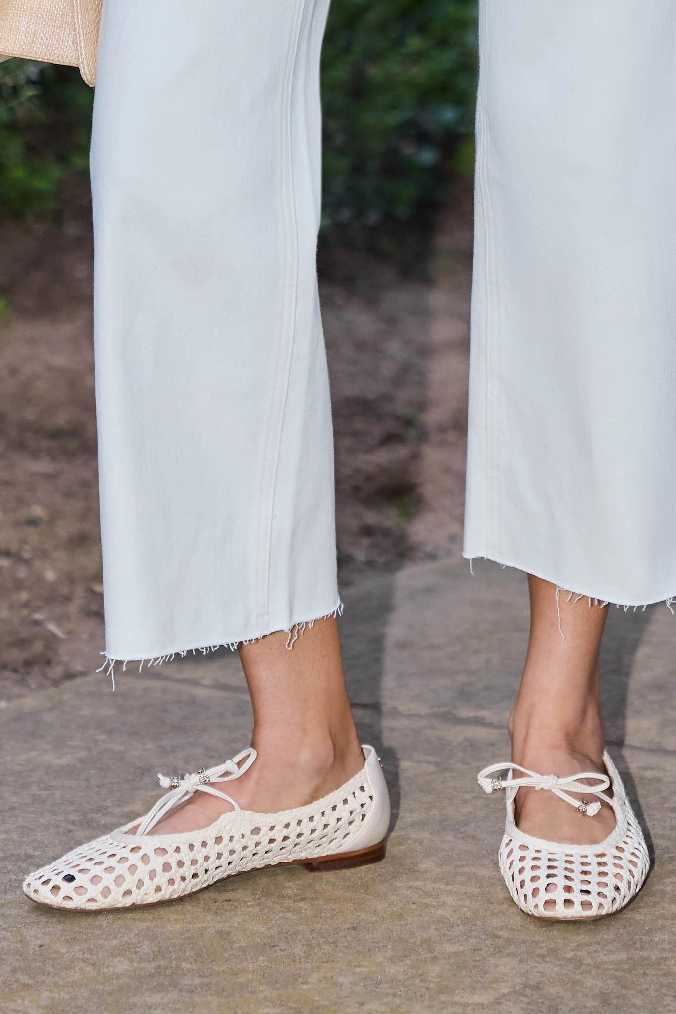 White woven flats worn with light blue jeans on a stone surface.