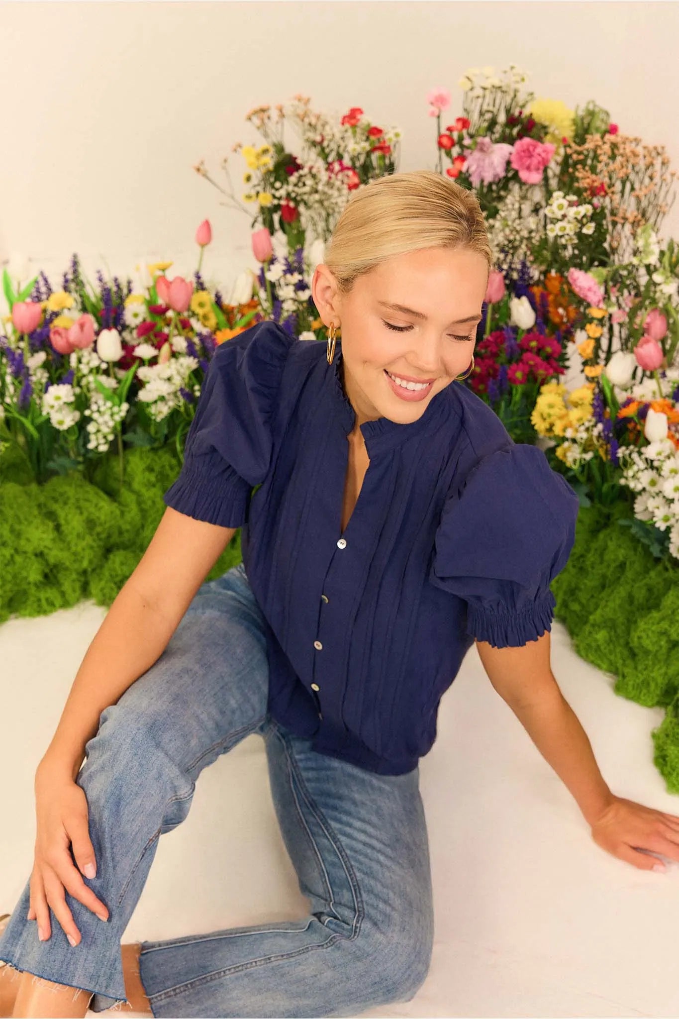 Woman in a navy blue blouse and jeans sitting in front of a colorful floral arrangement.