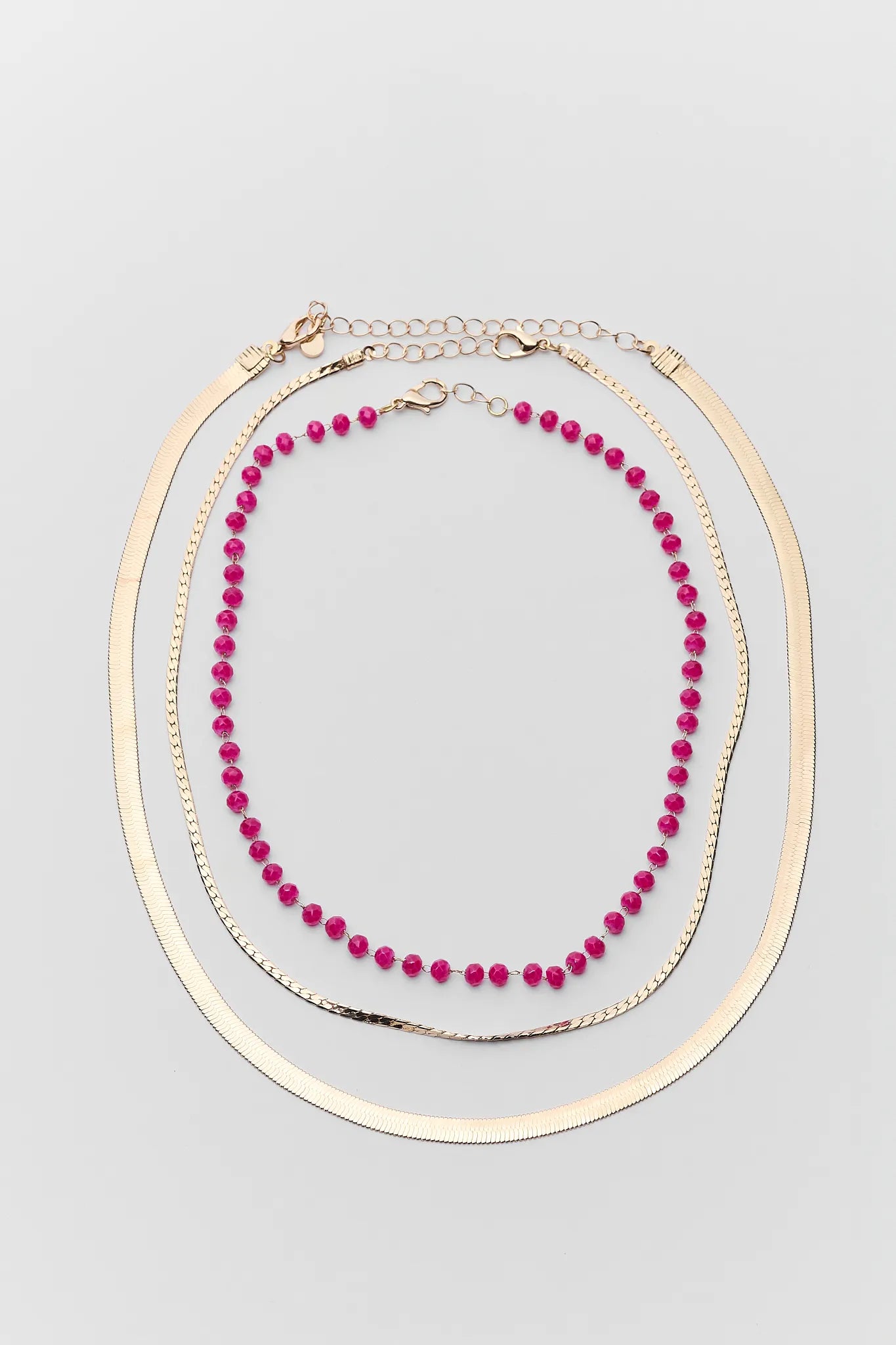 Two necklaces on a gray background, one pink beaded and one gold hoop.