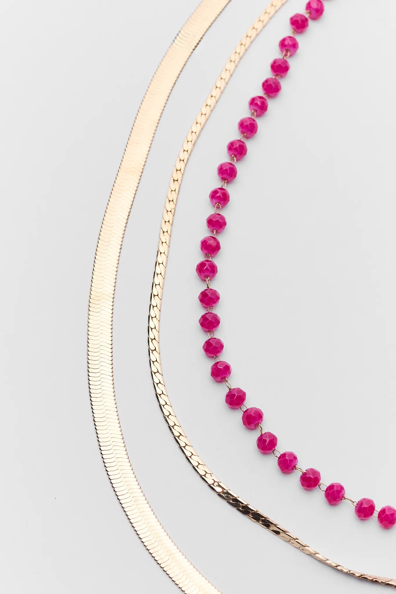 Two necklaces, one pink beaded and one gold chain, on a light gray background