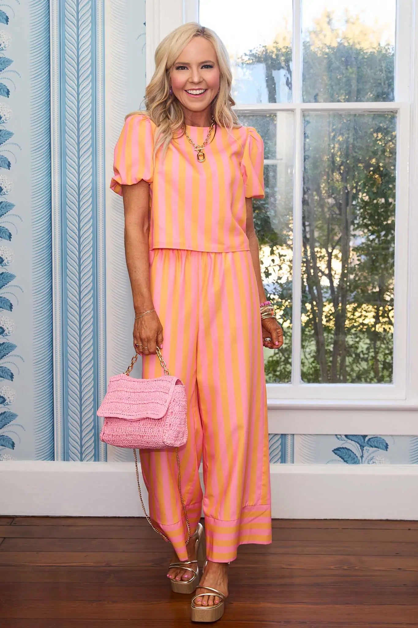 Woman in a pink and orange striped outfit holding a pink handbag indoors.
