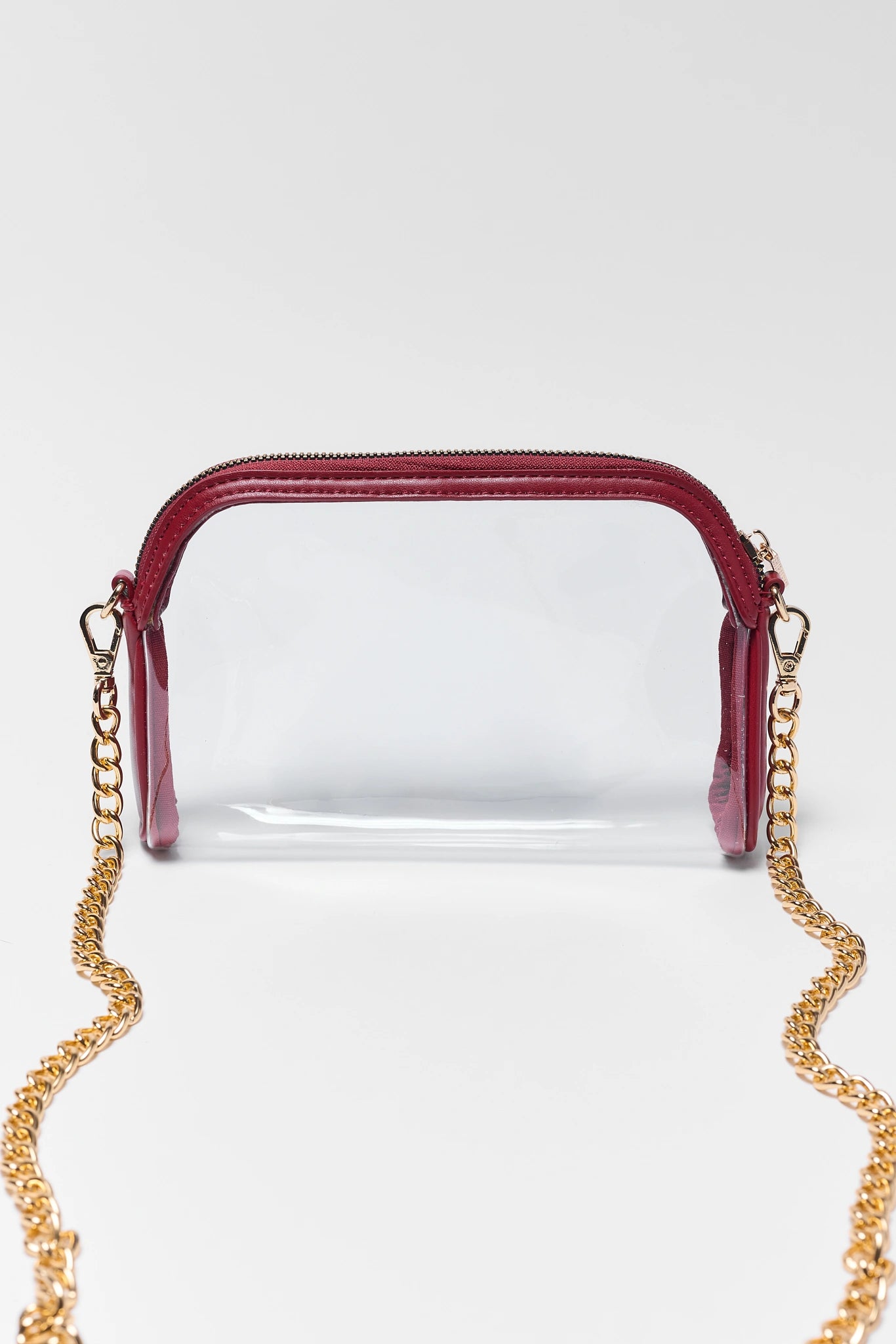 A clear plastic pouch bag with a burgundy top zipper and trim, featuring a gold-tone chain strap, shown against a light gray background.