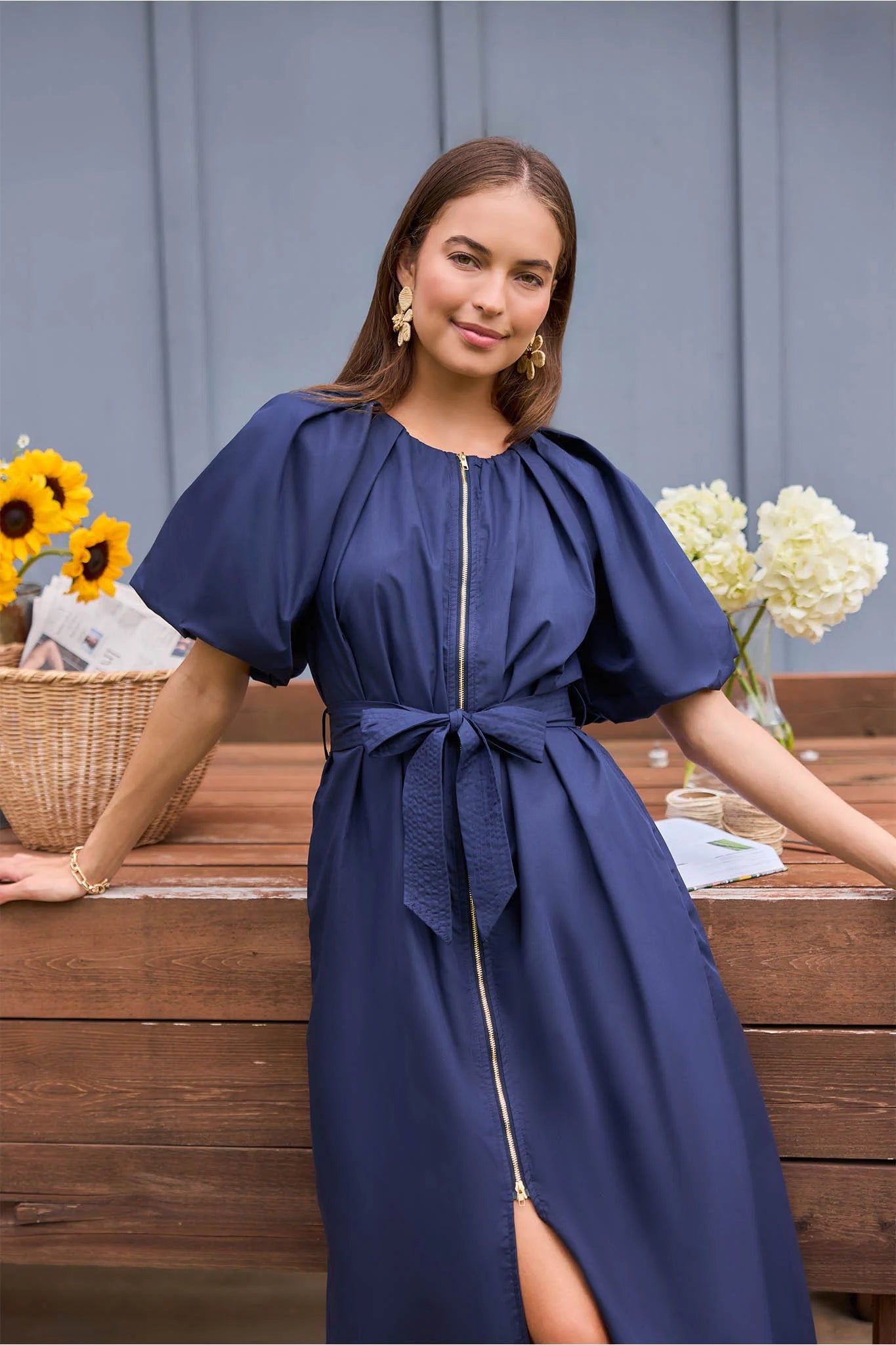 close up Woman in a blue dress sitting outdoors with flowers and a wooden table in the background