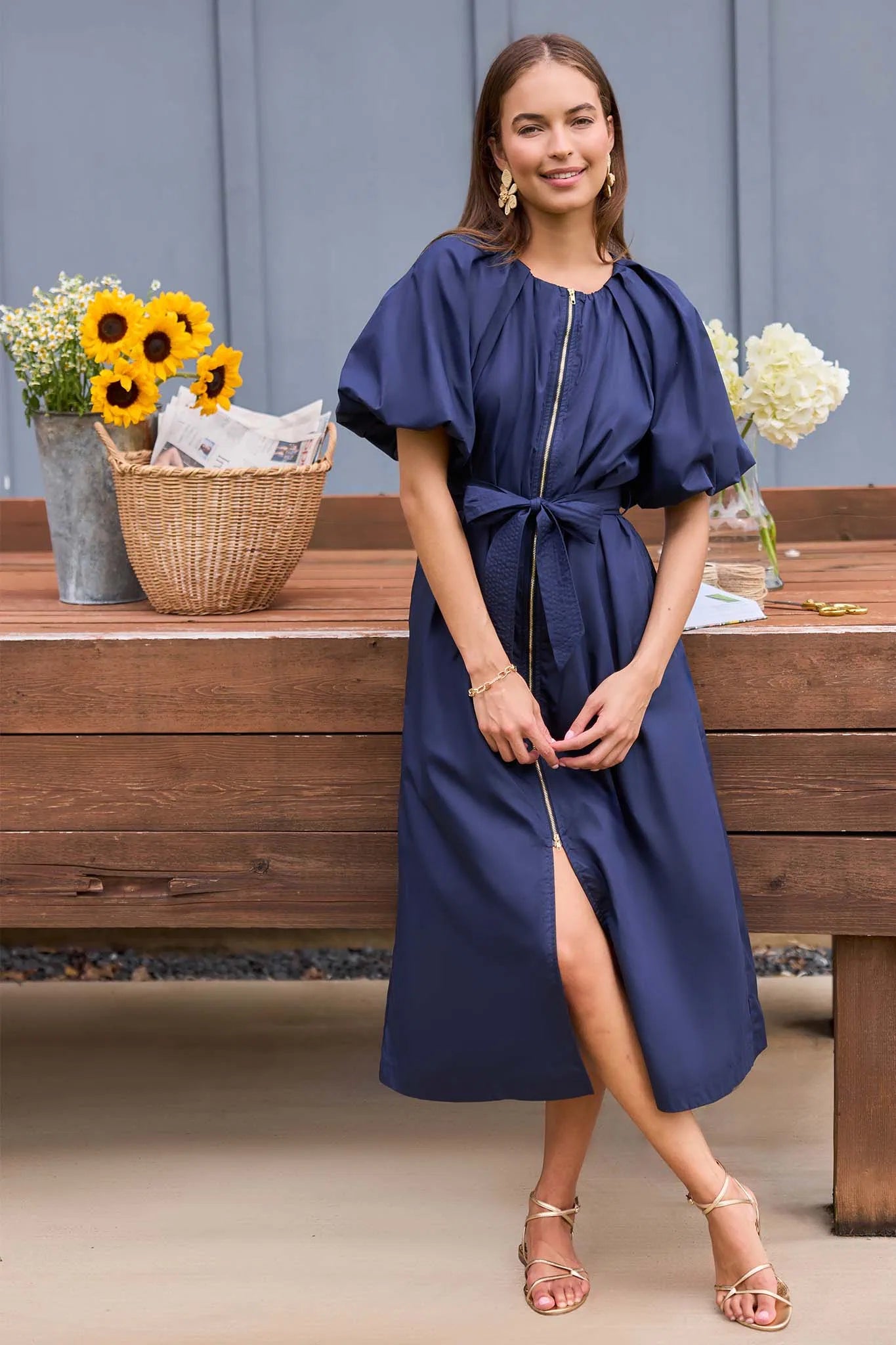 Woman in a blue dress standing in front of a wooden table with flowers.