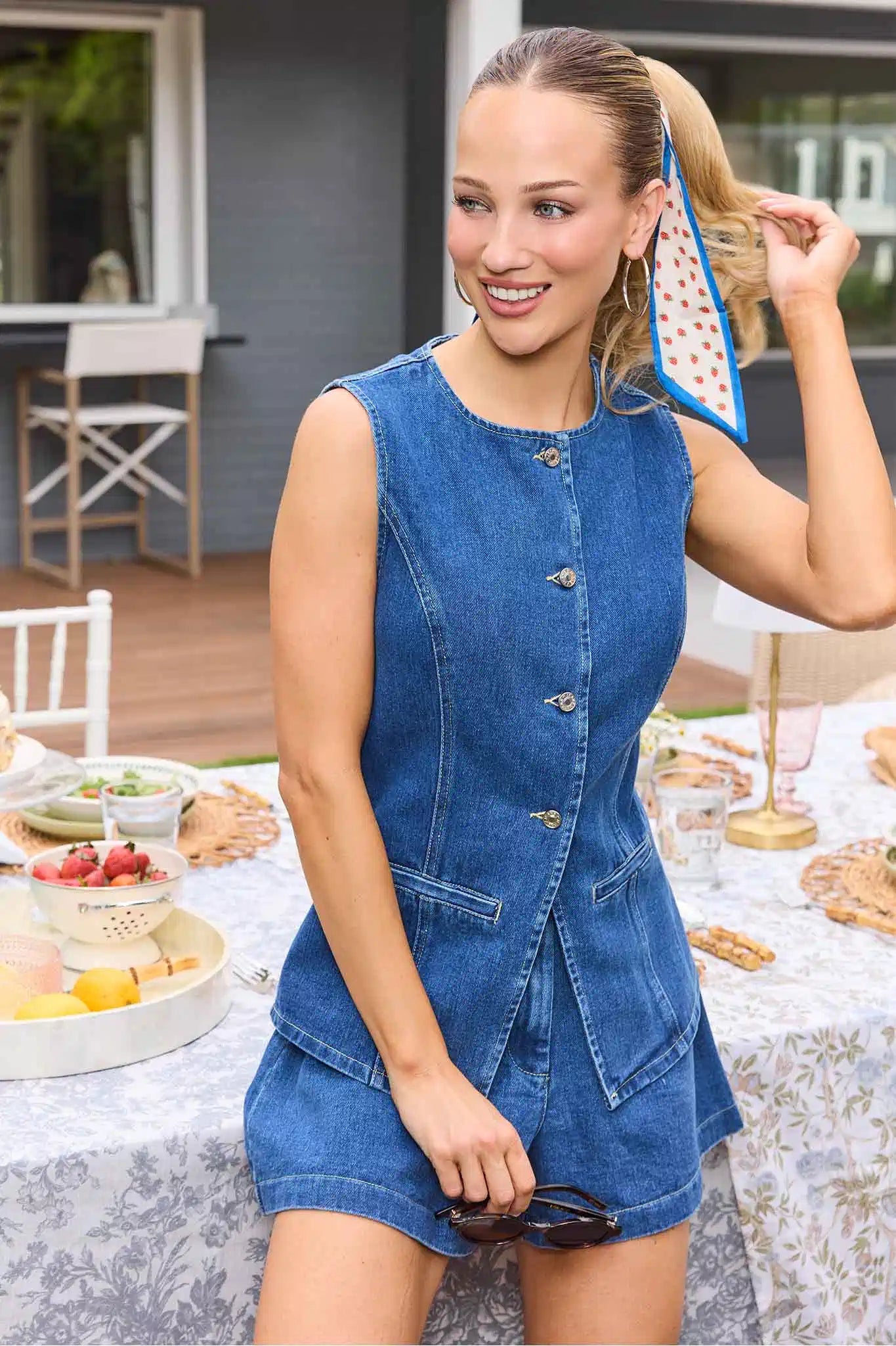 Woman in a denim dress standing outdoors at a table with food.