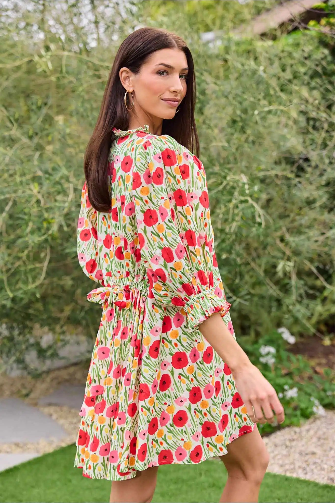 Woman wearing a floral dress standing outdoors with greenery in the background