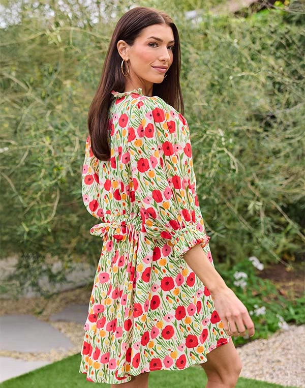Woman wearing a floral dress standing outdoors with greenery in the background