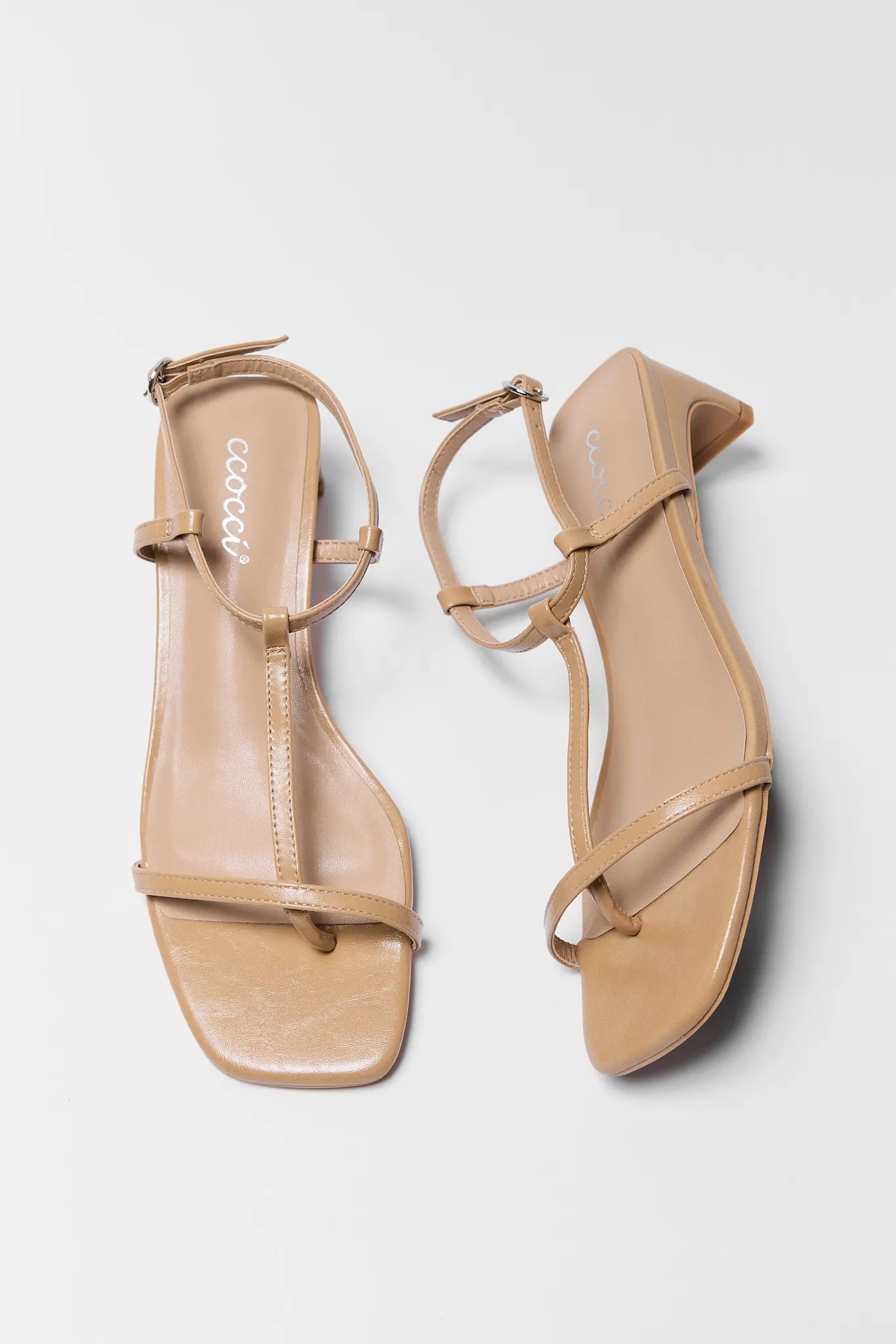 Pair of beige sandals with thin straps on a light gray background